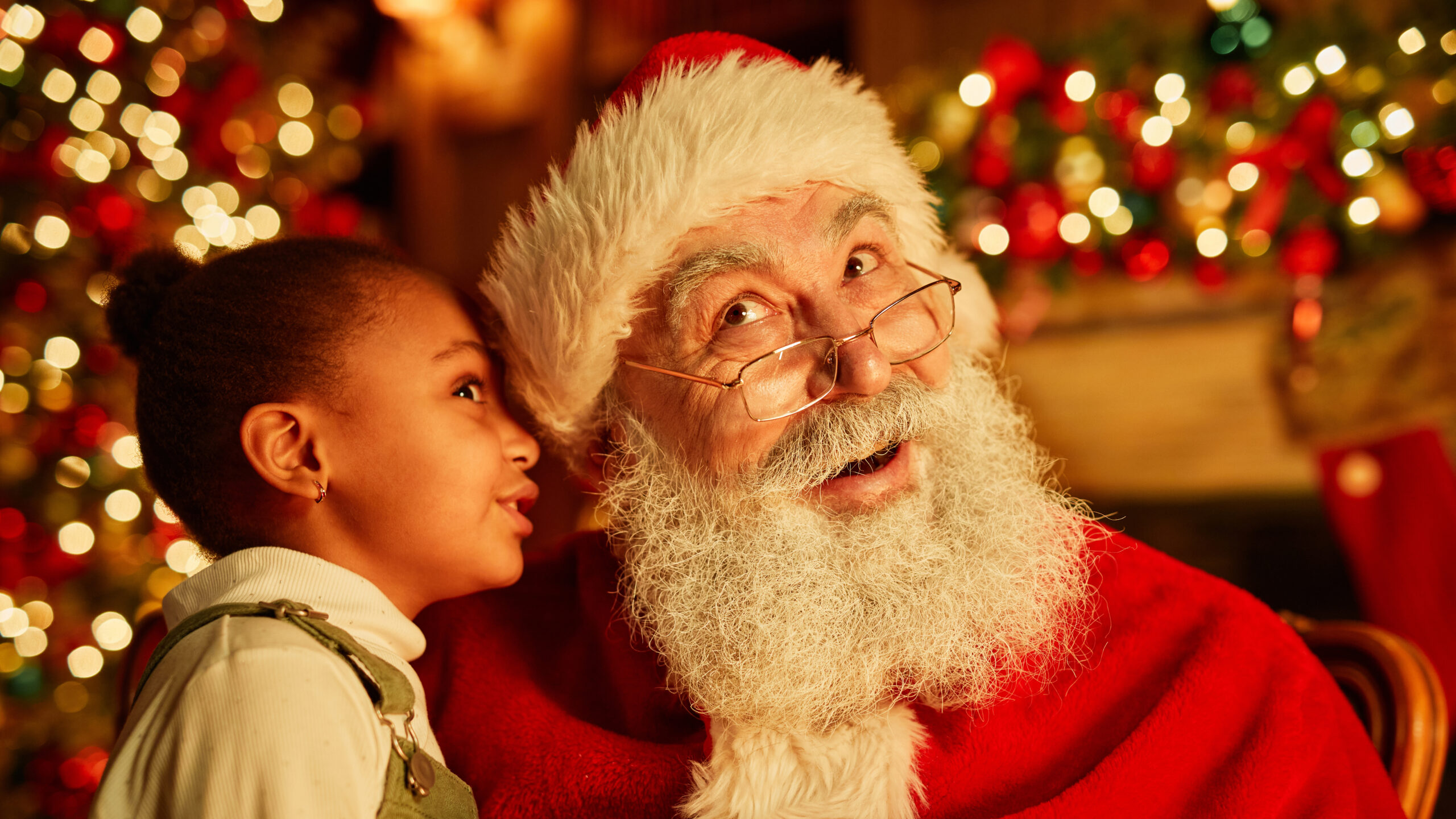 Portrait of cute black girl whispering secrets to Santa Claus on Christmas eve